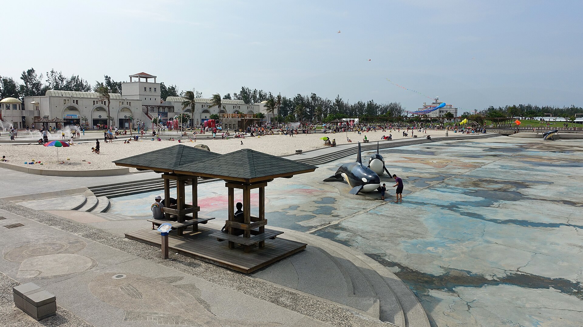 東石漁人碼頭親水區全景：沙池、虎鯨雕塑、涼亭與白色遊客中心建築